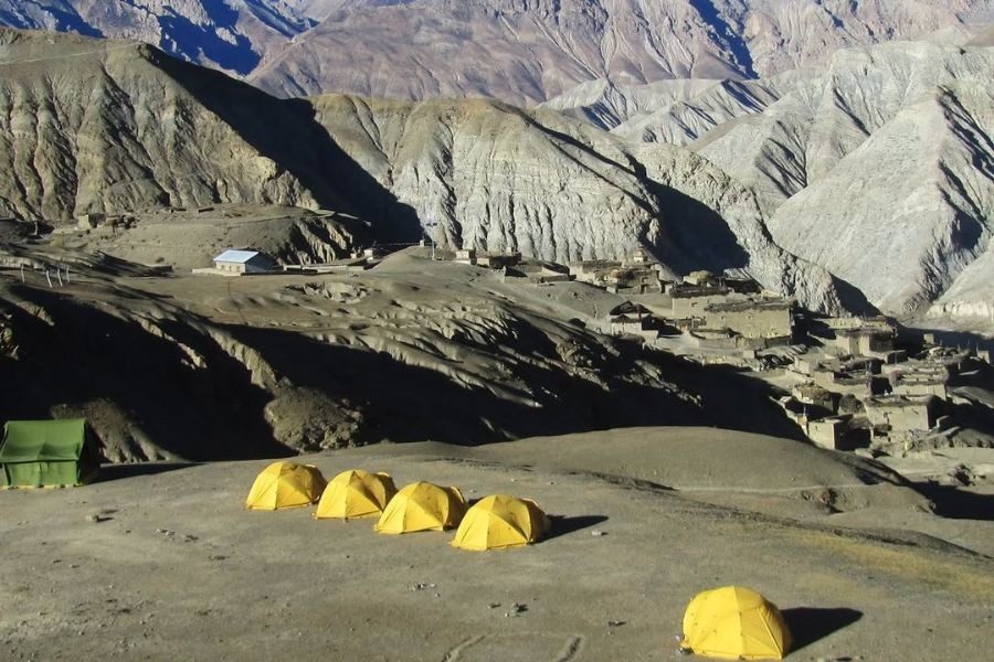 Yellow expedition tents set up in barren mountain landscape with traditional village in background